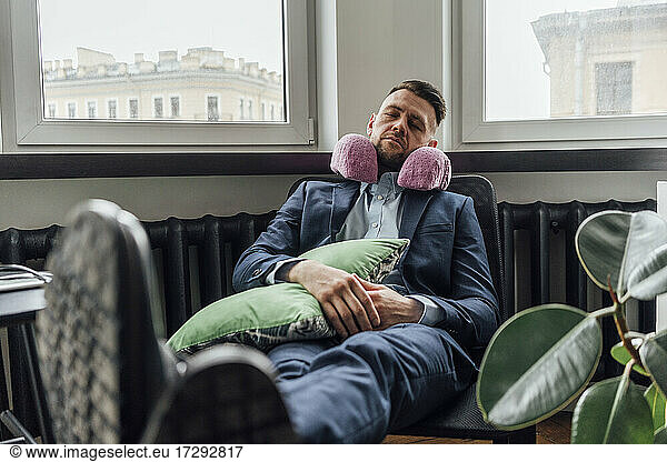 Businessman with neck pillow relaxing on chair in office