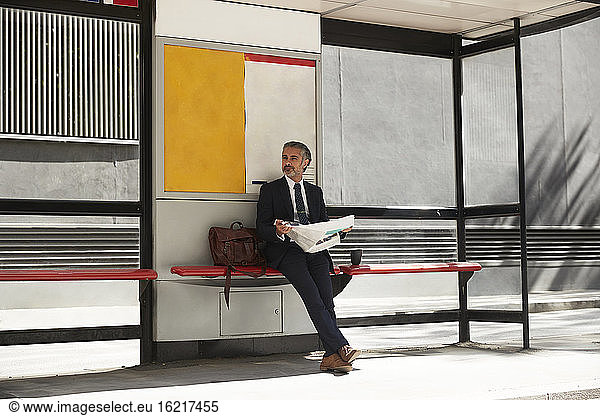 Businessman with newspaper waiting at bus stop