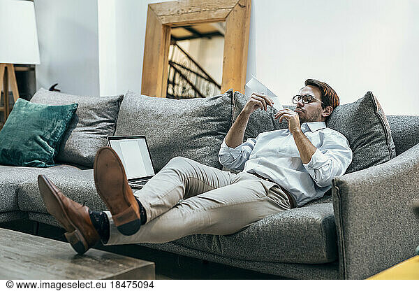 Businessman with paper airplane sitting on sofa at office