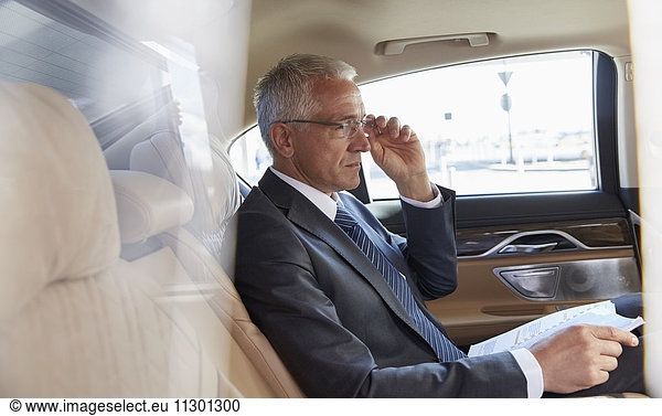 Businessman with paperwork riding in back seat of town car