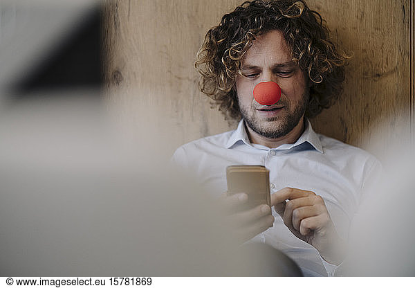 Businessman with red clown nose using cell phone in office