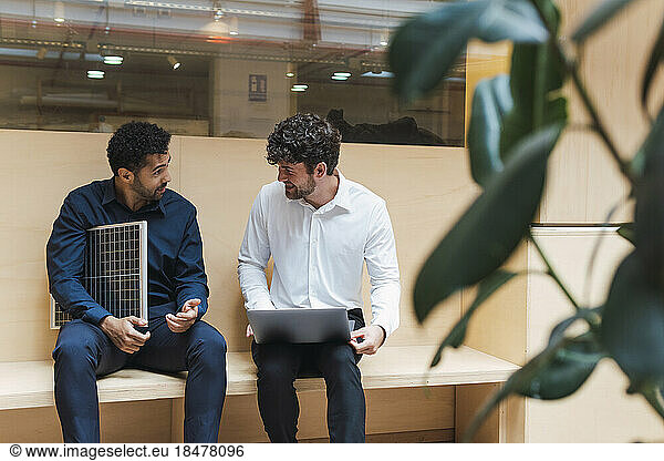 Businessman with solar panel and colleague with laptop talking in office