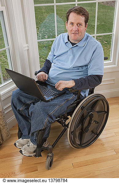 Businessman with spinal cord injury in a wheelchair working on a laptop with disabled hands