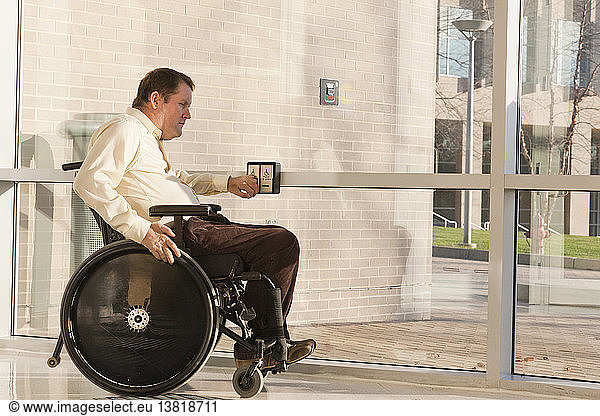Businessman with spinal cord injury in wheelchair using automatic door opener at office building entrance