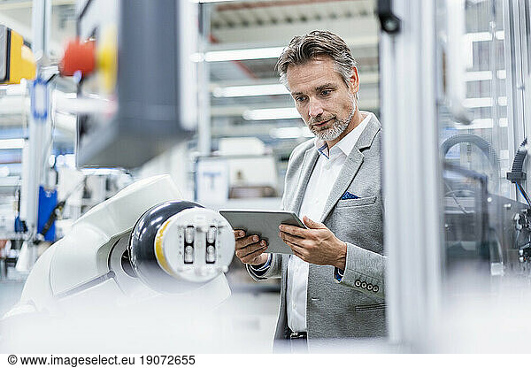 Businessman with tablet at assembly robot in a factory