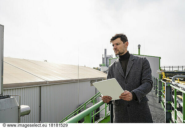Businessman with tablet PC standing at plant
