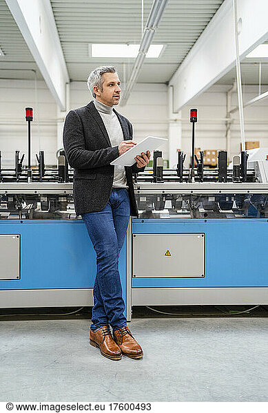 Businessman with tablet PC standing by machinery in factory