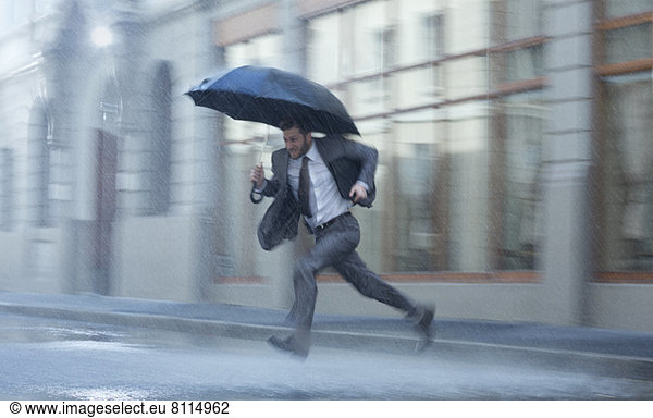 Businessman with umbrella running across rainy street