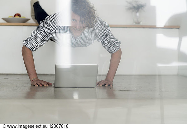 Businessman working from home with his laptop,  while doing a plank