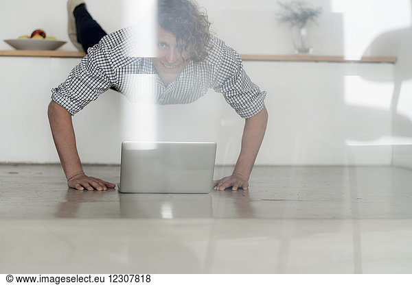 Businessman working from home with his laptop while doing a plank
