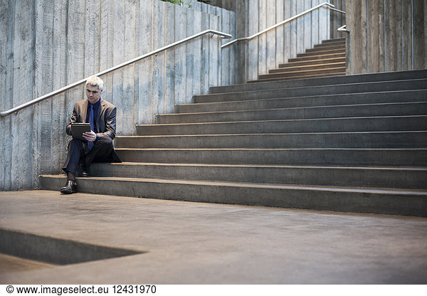 Businessman working on a notebook computer while sitting on the steps of a convention centre.