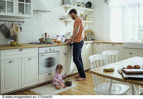Businessman working on laptop while daughter playing at kitchen