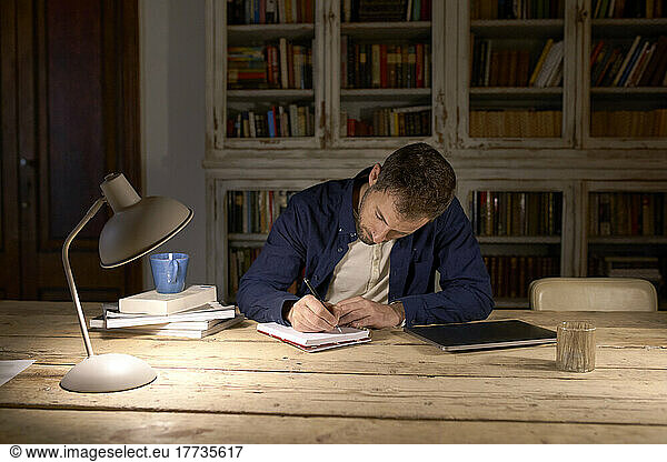 Businessman writing in diary on desk at home