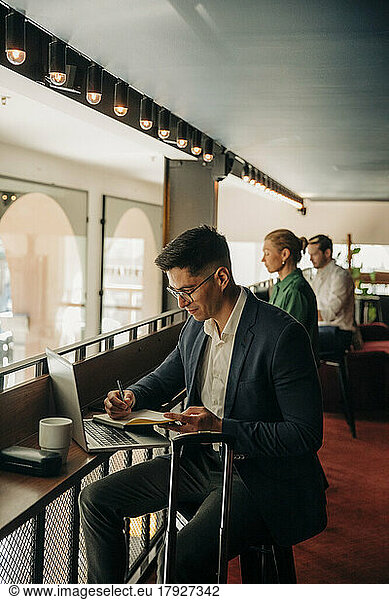 Businessman writing in diary while sitting with laptop at hotel