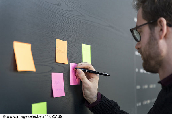 Businessman writing on adhesive note in office
