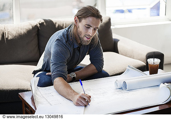 Businessman writing on blueprint in creative office