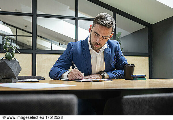 Businessman writing on clipboard at illuminated desk in creative office