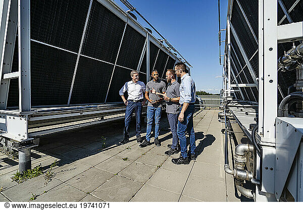 Businessmen and employees having a meeting on rooftop beside refrigeration installation