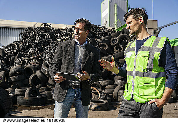 Businessmen discussing in front of tires on sunny day at recycling center