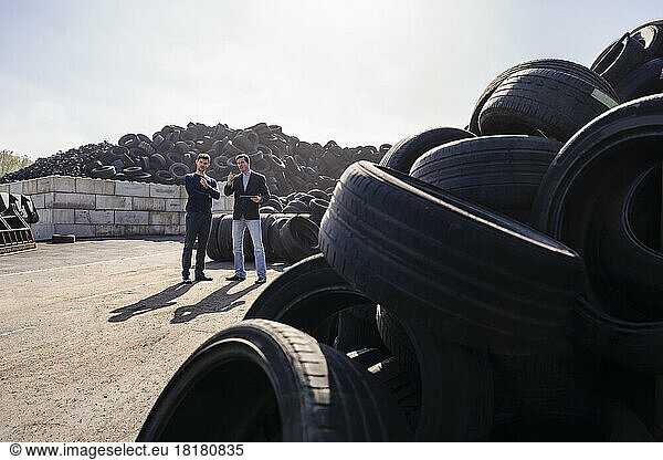 Businessmen discussing over heap of rubber tires at recycling plant