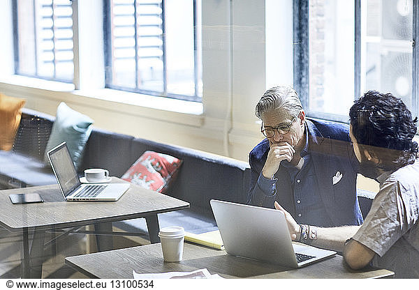 Businessmen discussing over laptop computer seen through window