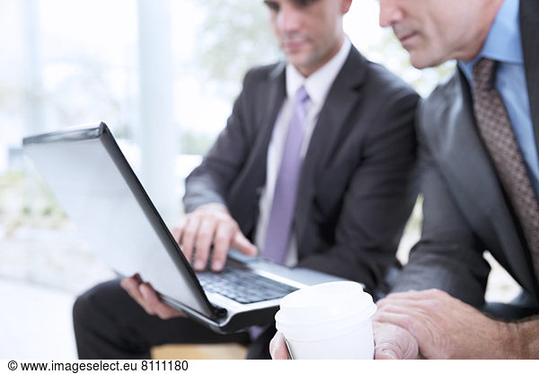 Businessmen drinking coffee and sharing laptop