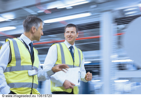 Businessmen in reflective clothing walking and talking in factory