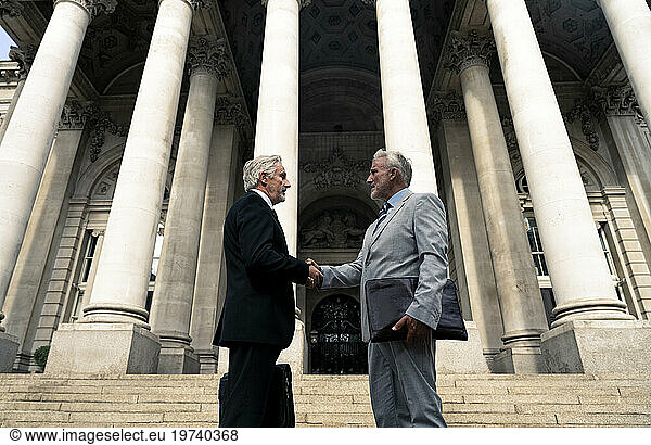 Businessmen shaking hands near architectural columns
