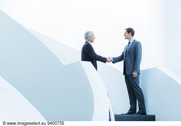 Businessmen shaking hands on staircase of office building