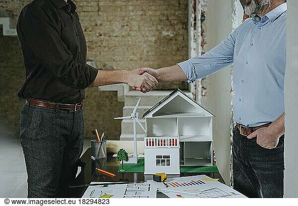 Businessmen shaking hands with house model on desk at table