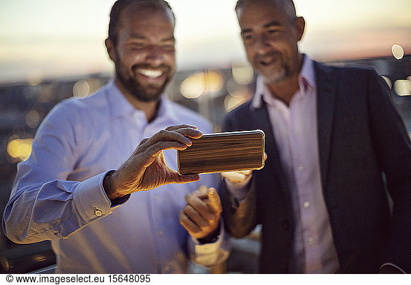 Businessmen taking selfie on smart phone at terrace during sunset