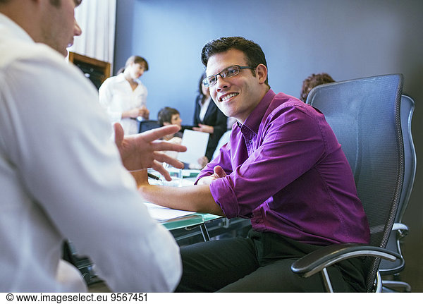 Businessmen talking during meeting in conference room with colleagues in background