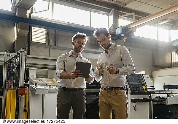 Businessmen using digital tablet while examining metal object at factory