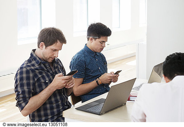 Businessmen using smart phones at desk in creative office