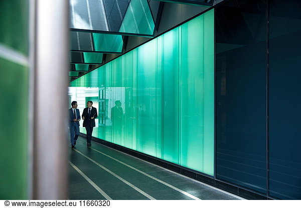 Businessmen walking through modern glass building  London  UK
