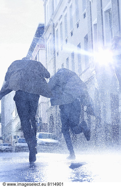 Businessmen with umbrellas running in rainy street