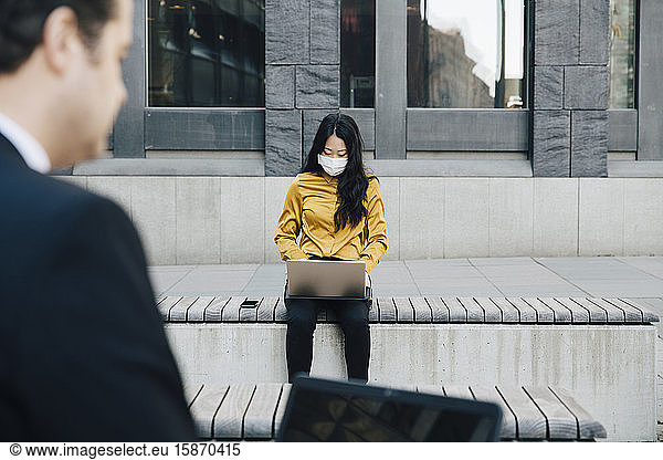 Businesspeople using laptop wearing face mask