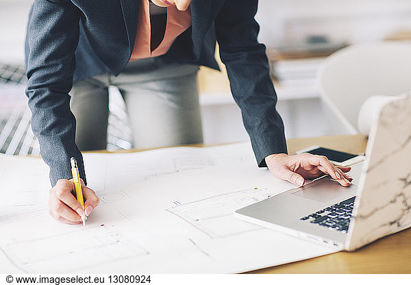 Businesswoman analyzing blueprint while standing at table