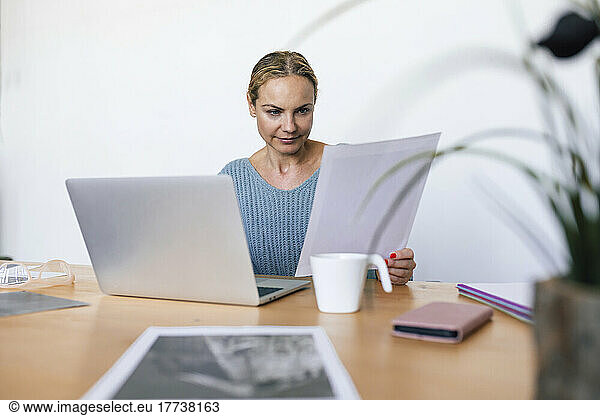 Businesswoman analyzing photograph sitting with laptop at home