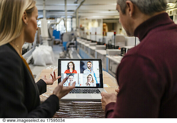 Businesswoman and businessman discussing with colleagues through video call on laptop in factory
