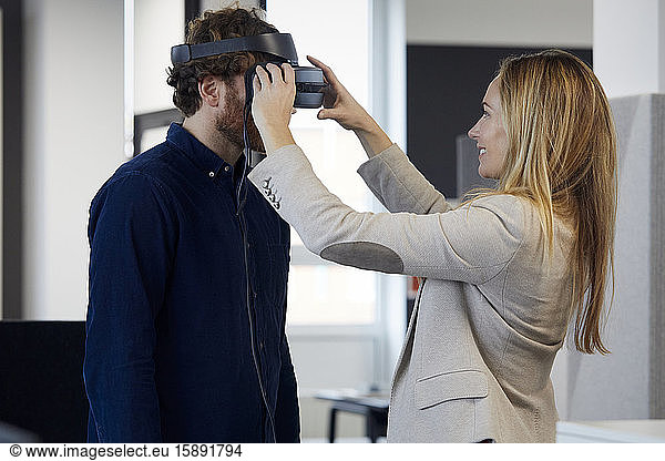 Businesswoman applying VR glasses on businessman in office