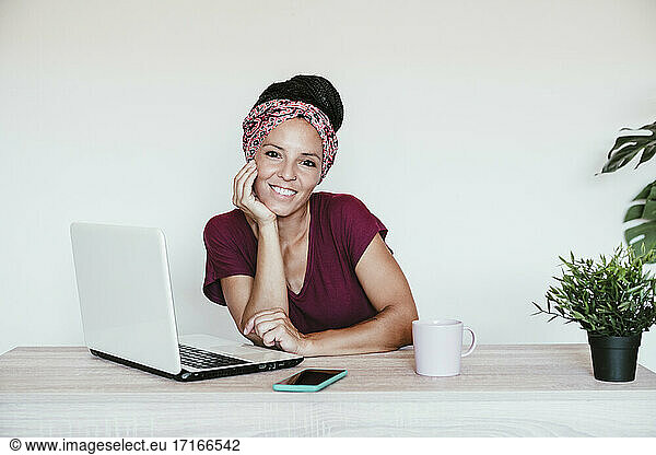 Businesswoman by laptop smiling with hand on chin at home