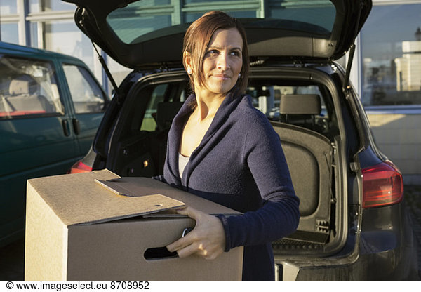 Businesswoman carrying cardboard box in front of car trunk
