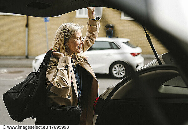 Businesswoman carrying luggage while opening car trunk