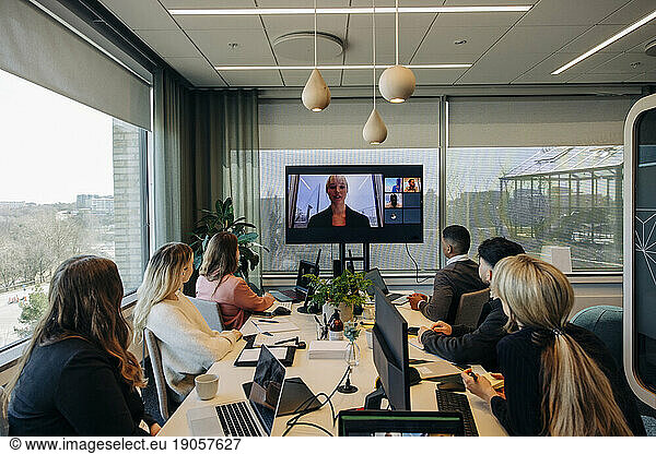 Businesswoman conducting video call with male and female colleagues sitting at desk in coworking office