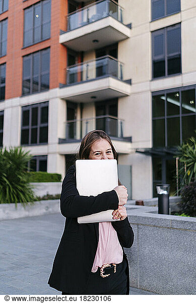 Businesswoman covering face with laptop in front of building