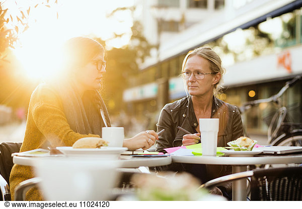 Businesswoman discussing with colleague about project on table at sidewalk cafe