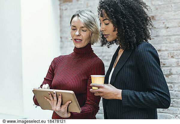 Businesswoman discussing with colleague over tablet PC in office