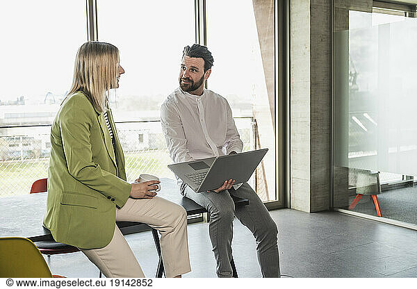 Businesswoman discussing with coworker holding laptop in office