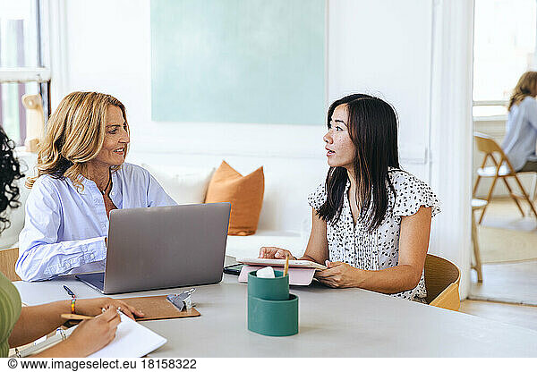 Businesswoman discussing with female colleague by laptop